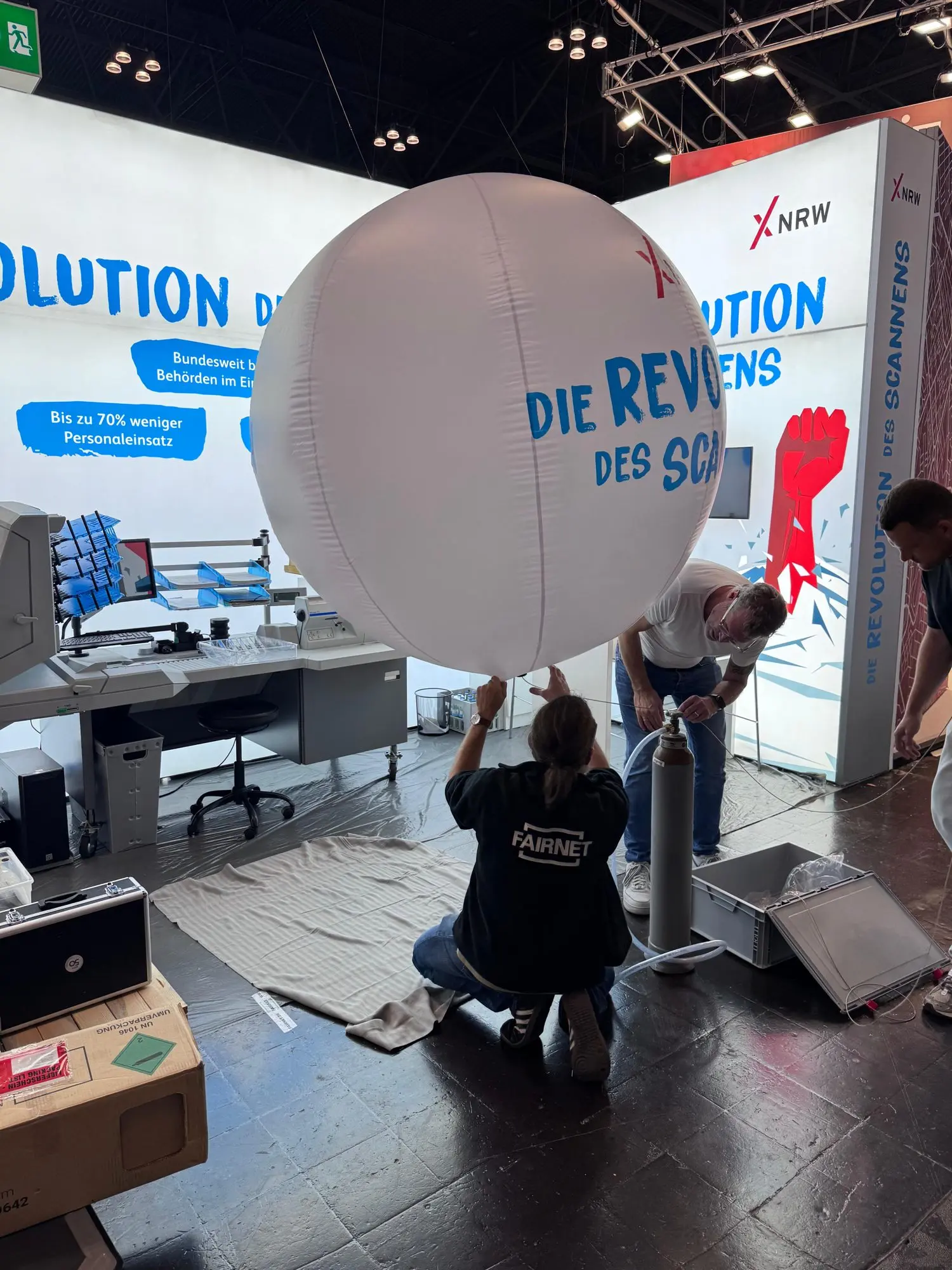 Das Messebau-Team befüllt beim Standaufbau einen großen weißen Ballon mit dem Schriftzug Die Revolution des Scannens