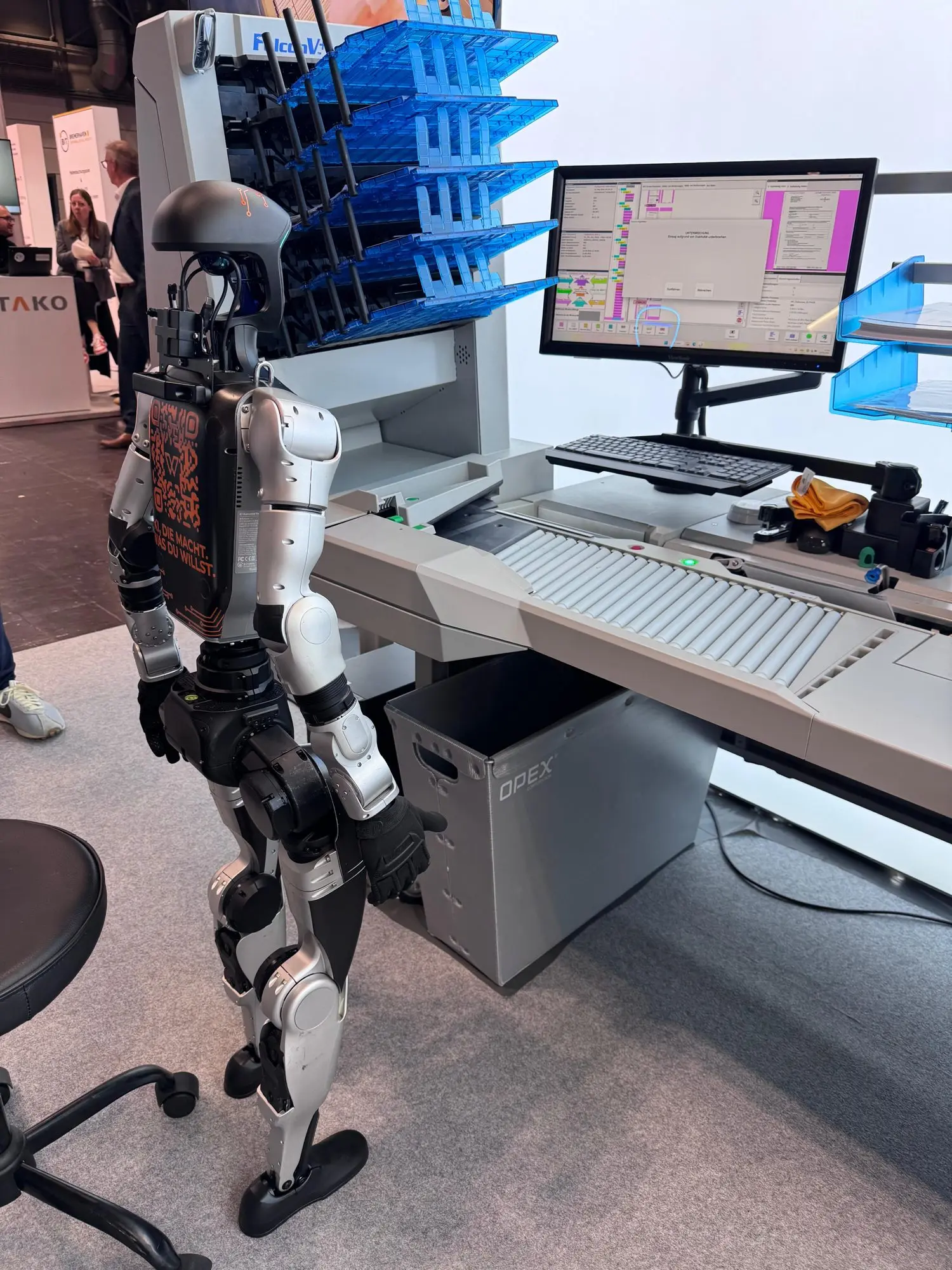 Humanoider Roboter steht neben dem OPEX-Scanarbeitsplatz am X-NRW-Stand