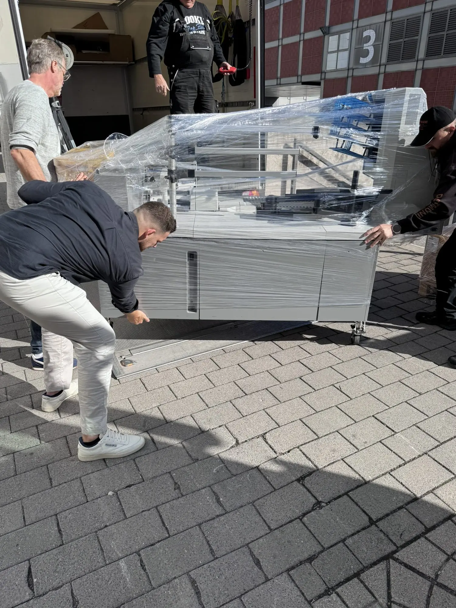 Das Team hebt den in Folie verpackten OPEX-Scanarbeitsplatz von der Ladefläche