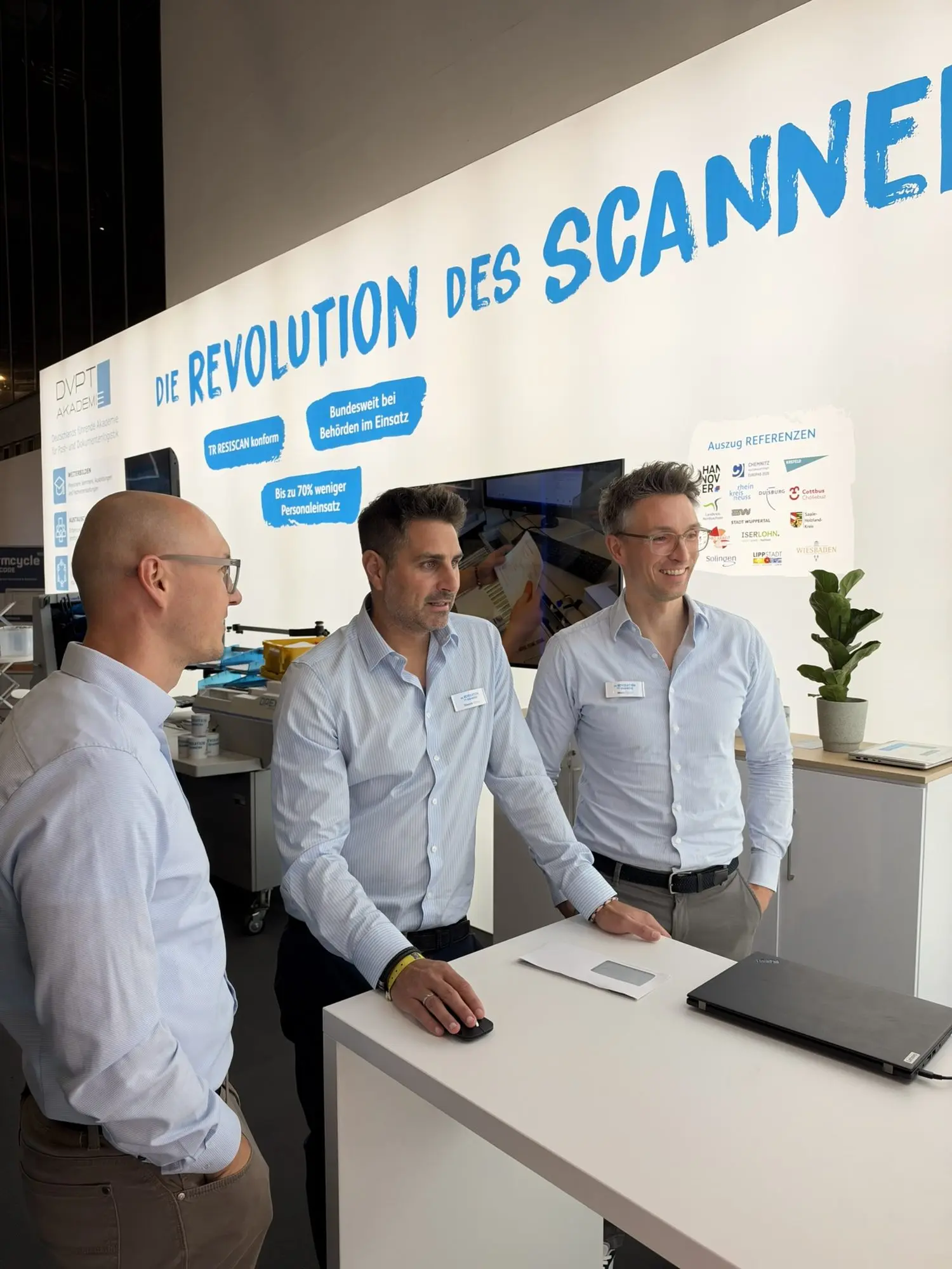 Drei Mitarbeiter von X-NRW am Beratungstresen vor der Wand Die Revolution des Scannens